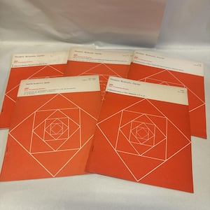 May include: A collection of vintage booklets with orange covers and white geometric designs. The booklets are labeled "Houston Scientific Center" and include text. The geometric design is a series of squares within squares.