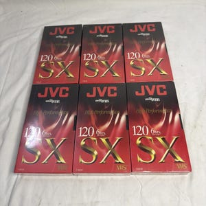 May include: Six JVC VHS video cassette tapes. The tapes are red with gold lettering and the JVC logo. Each tape is labeled "120 6hrs SX VHS". The packaging is in good condition.