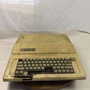 May include: A vintage Apple IIe computer, beige in color, with a full keyboard and the Apple logo. The computer shows signs of age and wear, with some keys missing. The model number "S-547" is visible on the top.