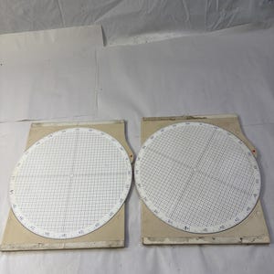 May include: Two vintage circular navigation plotters with a grid pattern and degree markings. The plotters are white with black grid lines and numbers, mounted on beige rectangular bases. The image is taken from a top-down perspective.