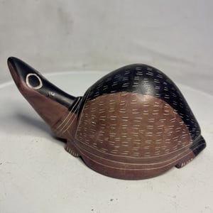 May include: A carved stone turtle figurine. The turtle has a black head and shell top, with a brown body and shell bottom. White lines are etched into the shell and body. The turtle is a decorative item.