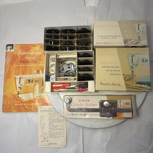 Pode incluir: Uma coleção de acessórios de máquinas de costura Singer vintage, incluindo uma caixa de bobinas, discos de moda e um ponto circular. A imagem também mostra um manual de instruções e uma caixa de acessórios Deluxe Zig-Zag.