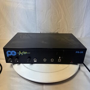 May include: A black audio amplifier with a rectangular metal chassis, featuring a blue logo, a yellow and blue waveform graphic, and the text PS-35. The front panel includes several black control knobs, input jacks, and a small red power light.