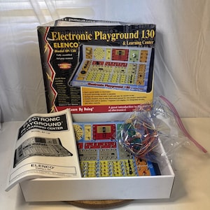 May include: Elenco Electronic Playground 130 and Learning Center model EP-130 kit in a box with a 164-page manual. The set includes a yellow and red circuit board base with various electronic components, a speaker, and a bag of colourful wires.