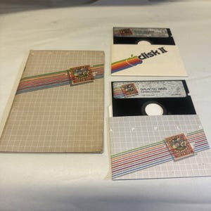 May include: Two floppy disks for the Apple II computer. The disk on the left is labeled "Galactic Wars" and the disk on the right is labeled "disk II". Both disks are in their original packaging.