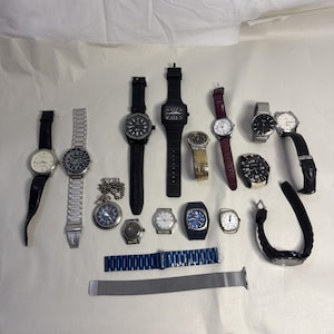 Peut inclure: Une collection de montres-bracelets et une montre de poche, présentées sur une surface blanche. Les montres présentent différents matériaux de bracelet, dont le cuir, le métal et le maillage. Les cadrans varient en style, avec des tons noirs, blancs et dorés. Certaines montres ont des lunettes noires.