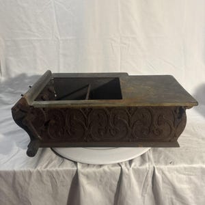 May include: An antique cast iron box, showing signs of age, with a hinged lid and decorative scrollwork. The box is rectangular, with a compartmented interior and a dark, rusty brown colour. The box is likely of European origin.