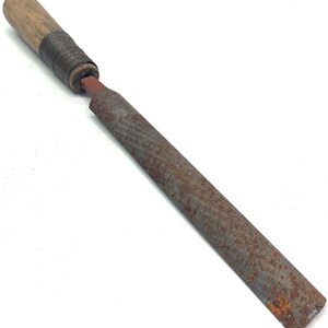 May include: A metal file with a wooden handle. The file has a rectangular shape with a textured surface and a rusty appearance. The handle is made of light-colored wood and is attached to the file with a metal band.