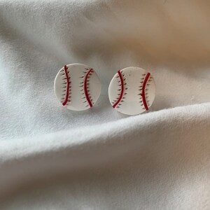 May include: A pair of white baseball earrings with red stitching.
