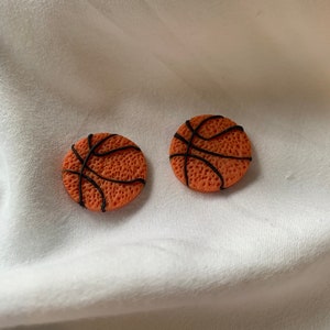 May include: A pair of orange and black basketball-shaped earrings. The earrings are made of polymer clay and have a textured surface.