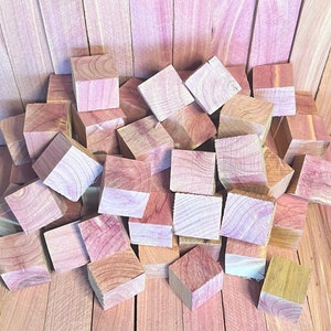 May include: A pile of small, square, wooden blocks made of cedar wood. The blocks are a light reddish-brown color and have a natural wood grain pattern. The blocks are arranged in a random pile, with some blocks stacked on top of others.