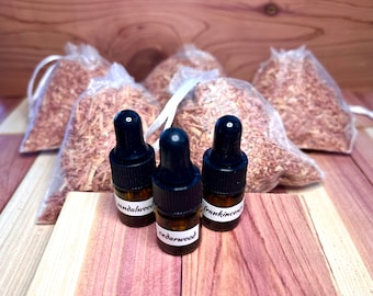 May include: Three small glass bottles with black dropper tops and labels. The bottles are filled with essential oils and labeled "sandalwood", "cedarwood", and "frankincense". The bottles are sitting on a wooden surface with several small mesh bags filled with wood shavings.