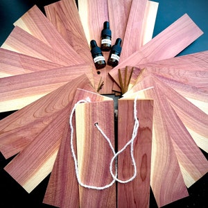 May include: A set of cedar wood planks with a natural wood grain pattern. The planks are arranged in a circle around four small bottles of essential oil. The bottles are black with white labels and are filled with a clear liquid.