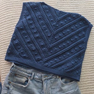 May include: A blue crochet top with a textured pattern and a ribbed hem. The top is paired with light blue denim shorts. The crochet design features a chevron pattern with openwork details.