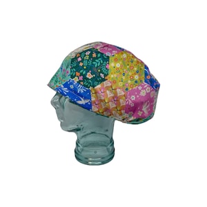 May include: A colorful patterned surgical scrub hat with a patchwork design featuring various floral and geometric patterns in shades of pink, blue, green, and yellow.