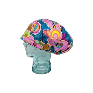May include: A teal blue, pink, orange, and yellow patterned surgical scrub hat with a whimsical design featuring clouds, birds, and flowers.