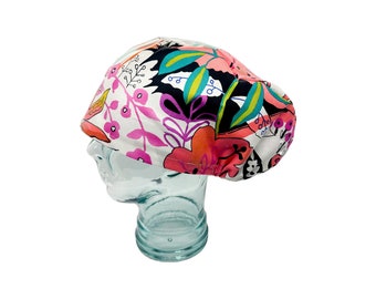 May include: A white scrub hat with a colorful floral print featuring pink, orange, green, and black. The hat is on a mannequin head.