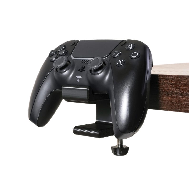 PlayStation 5 controller sits upright on the controller and headphone holder clamped to the side of a desk.