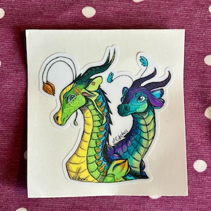 Peut inclure: Un autocollant repr&eacute;sentant deux t&ecirc;tes de dragon stylis&eacute;es. Le dragon de gauche est vert et jaune avec une longue antenne termin&eacute;e par une feuille. Le dragon de droite est bleu et violet avec des antennes plus petites, des cornes et des &eacute;cailles.