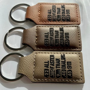 May include: Three leather keyrings with silver key rings. Each keyring has a rectangular tag with the text "22 ALL 380 FASTER THAN 9mm 40 DIALING 45 911" engraved in black.