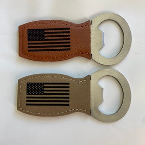 Puede incluir: Dos abridores de botellas con mango de cuero y un abridor de metal. El mango de cuero tiene un diseño de bandera estadounidense, uno es marrón y el otro es beige.