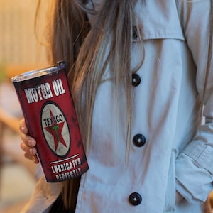 May include: A red and white vintage-style metal tumbler with the text "Motor Oil" and "Texaco" with a red star logo. The text "Lubricates Perfectly" is below the logo.