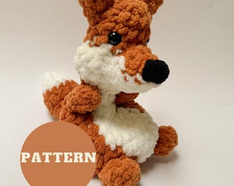 May include: A crocheted fox plush toy with orange and white fur. The fox is sitting with its tail curled behind it. The toy has black eyes and a black nose. The word "PATTERN" is written in white letters on a brown circle.