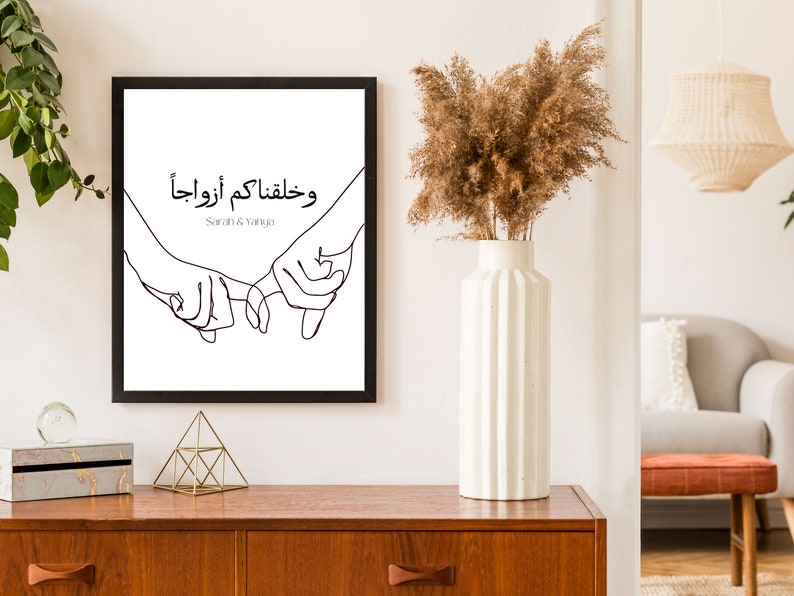 May include: Black and white line art print of two hands holding each other with the Arabic text "وخلقناكم أزواجا" and the names "Sarah & Yanuja" below.
