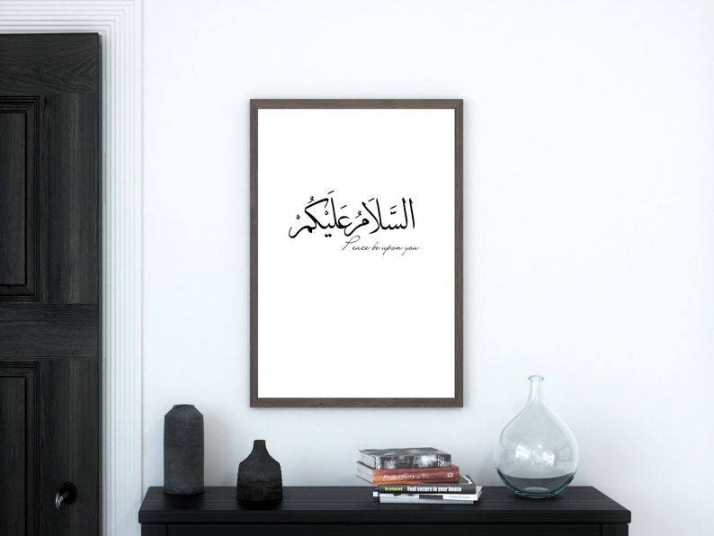 May include: A framed print with Arabic calligraphy that reads "Peace be upon you" in English. The print is hanging on a white wall in a modern interior.