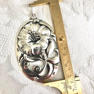 May include: A silver pendant featuring a detailed floral design with a single flower and leaves. The pendant is approximately 5 cm in length and has a loop at the top for attaching a chain.