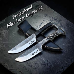 Puede incluir: Dos cuchillos grabados a medida con fundas de cuero. Las hojas son plateadas con los nombres "Joshua" y "Michael" grabados. Los mangos son negros y plateados. La imagen también incluye el texto "Professional Fiber Laser Engraving".