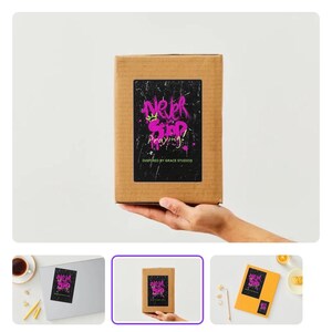 Puede incluir: Una caja de cartón marrón con una etiqueta negra con el texto "Never Stop Praying!" en letras rosas y blancas de estilo grafiti. La etiqueta también incluye el texto "Inspired by Grace Studios."
