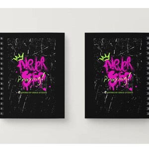 Puede incluir: Dos cuadernos negros con espiral con el texto "Never Stop Praying!" en estilo graffiti rosa y verde. Un gráfico de corona verde está encima del texto. Los cuadernos están sobre un fondo blanco.