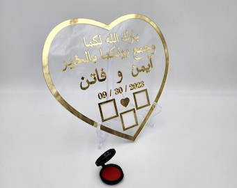 May include: A clear heart-shaped plaque with a gold border and Arabic text. The plaque has three empty photo frames and the date 09/30/2023. A red ink pad is in the foreground.