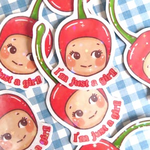 Può includere: Una collezione di adesivi con un personaggio dei cartoni animati con una testa a forma di ciliegia e la scritta "I'm just a girl!". Gli adesivi hanno uno schema di colori rosso e verde con un bordo bianco e un effetto glitter.