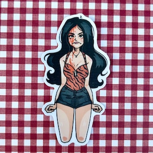 May include: A die-cut sticker featuring an illustrated character with long black hair, wearing an orange and black tiger-striped halter top and dark denim shorts. The character has red markings on their face and chest, and a small silver dog tag necklace.