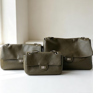 May include: Three olive green leather shoulder bags of varying sizes, each featuring a textured surface, a fold-over flap, and a silver-toned rectangular turn-lock closure. The bags are arranged with the smallest in front and two larger ones behind.