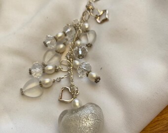 May include: A silver charm keychain with a large heart-shaped glass charm. The glass charm is silver with a sparkly finish. The keychain also has smaller charms, including hearts, beads, and a small silver charm.