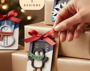 Könnte beinhalten: Ein Set aus 5 Designs mit rechteckigen Geschenkanhängern mit Feiertagsmotiven, darunter ein Pinguin mit grünem Schal und ein Schneemann mit orangefarbenem Schal. Jeder Anhänger ist mit einer roten Satinschleife versehen und an einer Goldbox.