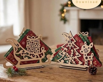 Puede incluir: Dos servilleteros de madera cortados con láser con diseños festivos. Uno tiene forma de trineo con un regalo y el otro es un árbol de Navidad con un reno. Ambos contienen servilletas rojas y verdes. El texto dice Digital Download.