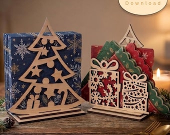 May include: Two laser-cut wooden napkin holders featuring holiday designs. One holder is shaped like a Christmas tree, and the other features two gift boxes with snowflake and ornament cutouts. The text Digital Download appears in an oval.