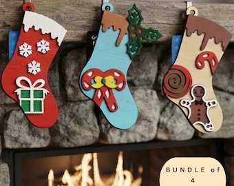 May include: Three wooden Christmas stocking ornaments hanging from metal hooks. The first is red with white snowflakes and a green gift. The second is light blue with candy canes and holly. The third is tan with a gingerbread man and candy.