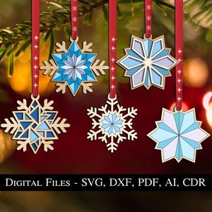 Pode incluir: Cinco designs diferentes de flocos de neve para cortar e fazer artesanato. Os flocos de neve são azuis e brancos com um padrão geométrico. Os flocos de neve estão pendurados em uma fita vermelha.