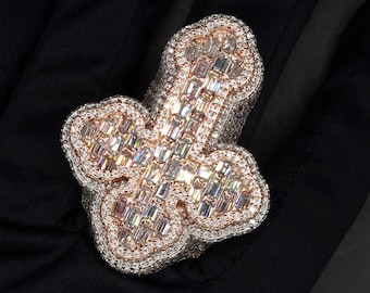 May include: A large, rose gold ring with a clover design. The ring is set with many clear, baguette-shaped diamonds.