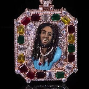 Puede incluir: Colgante de oro rosa con un retrato de un hombre con rastas, rodeado de piedras preciosas de colores y cristales transparentes. El colgante tiene forma rectangular.