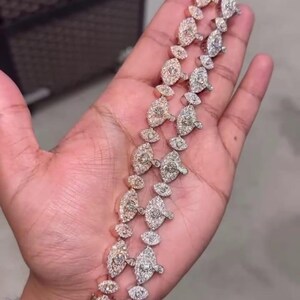 May include: Two diamond bracelets with a floral design are displayed in a hand. The bracelets are made of gold and silver, with each link featuring a central diamond surrounded by smaller stones. The bracelets are a luxurious accessory.