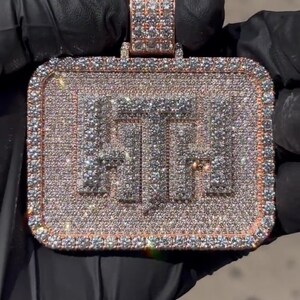 K&ouml;nnte beinhalten: Ein goldener Anh&auml;nger in rechteckiger Form mit den Buchstaben "FTF", die mit Diamanten besetzt sind. Der Anh&auml;nger ist von einem Rand aus kleineren Diamanten umgeben.