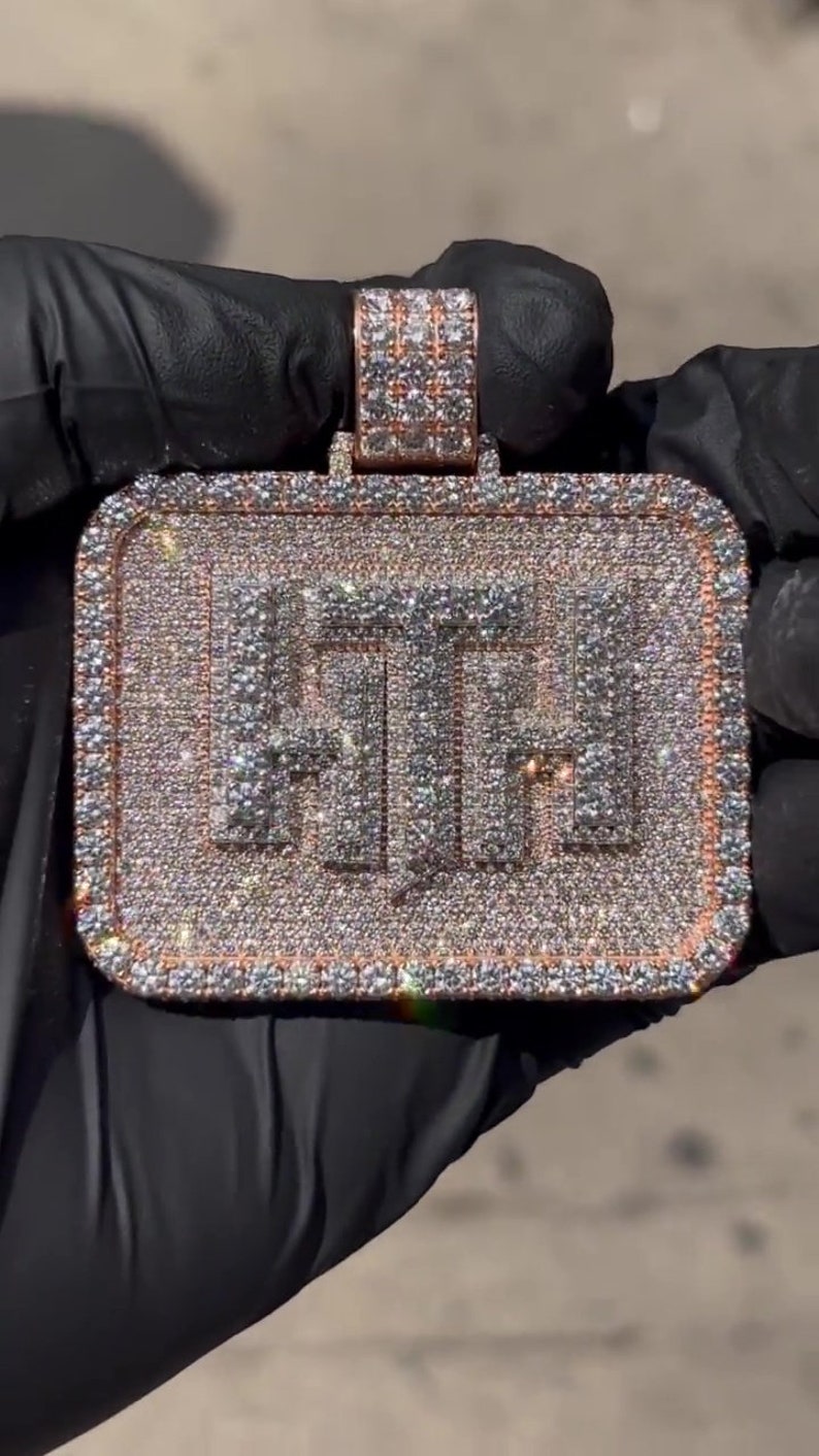 K&ouml;nnte beinhalten: Ein goldener Anh&auml;nger in rechteckiger Form mit den Buchstaben "FTF", die mit Diamanten besetzt sind. Der Anh&auml;nger ist von einem Rand aus kleineren Diamanten umgeben.