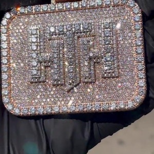 K&ouml;nnte beinhalten: Ein goldener Anh&auml;nger mit quadratischer Form, bedeckt mit kleinen Diamanten, die das Wort "HUF" in fetter Schrift buchstabieren.