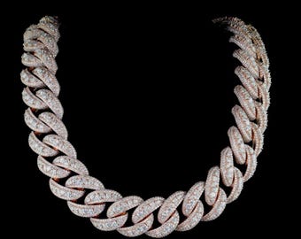 May include: A rose gold chain necklace with a cuban link design. The links are encrusted with numerous small, clear gemstones, creating a sparkling effect. The necklace is set against a black background.